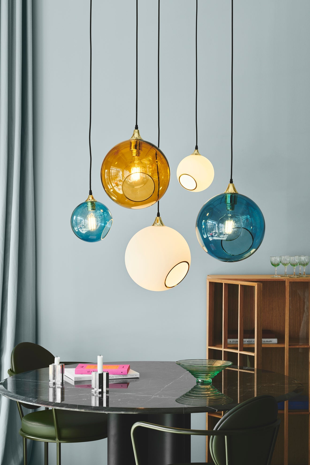 Rund lampa i blått glas och med en avskuren bit med guldkant för en skymt av glödlampan. Sockel och rosett är guldfärgade och sladden är av svart tyg.