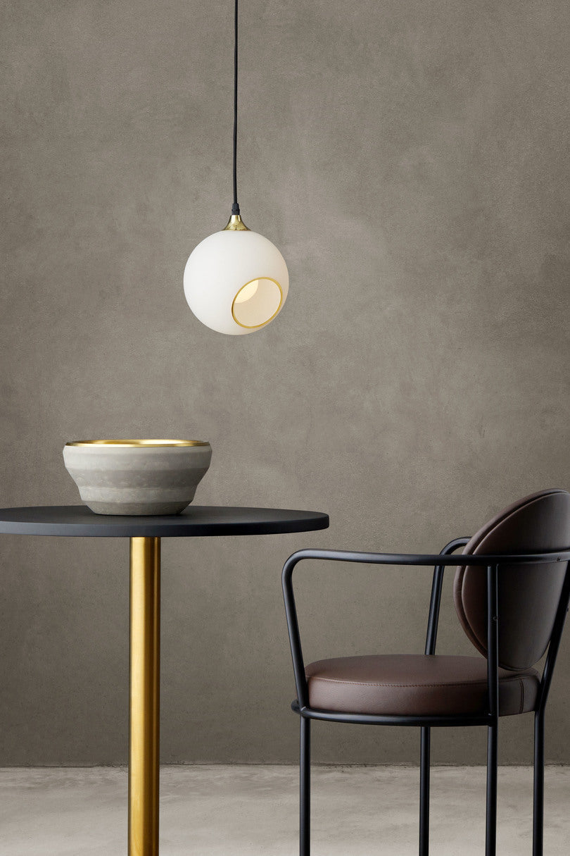 Rund lampa i vitt glas och med en avskuren bit med guldkant som ger en skymt av glödlampan. Sockel och rosett är guldfärgade och sladden är av svart tyg.