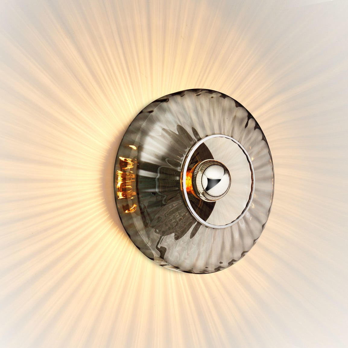Rund vägglampa i rökfärgat veckat glas som skapar ett ljusspel på väggen.