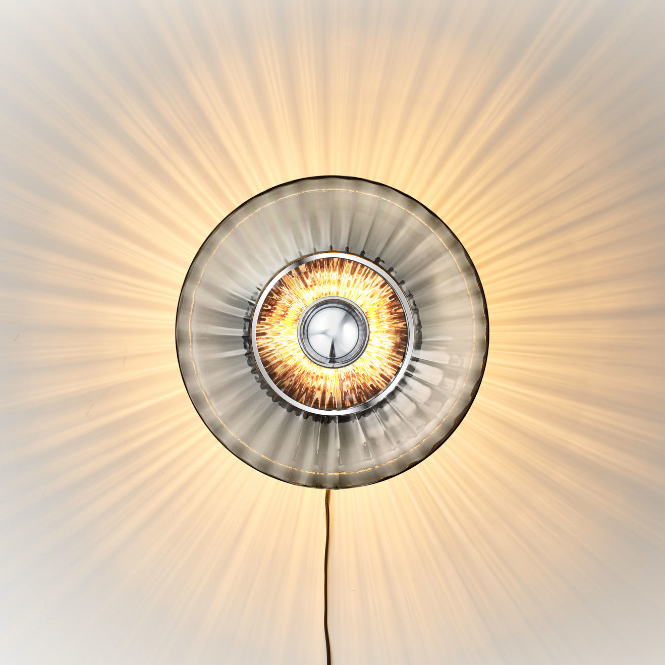 Rund vägglampa i rökfärgat veckat glas som skapar ett ljusspel på väggen.