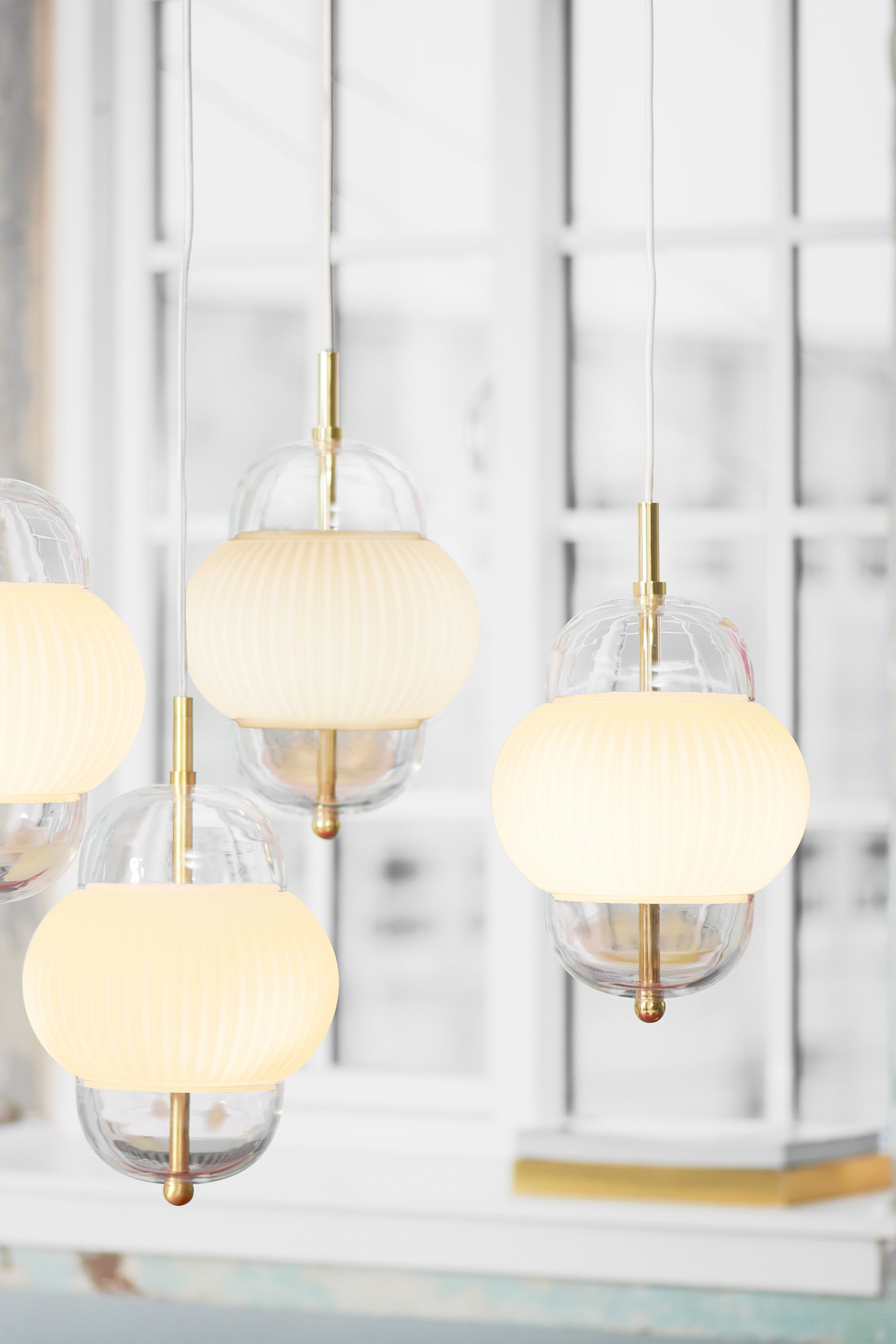Lampa i klarglas och matt vitt veckat glas. Dessutom har lampan detaljer i mässing och en vit textilkabel.