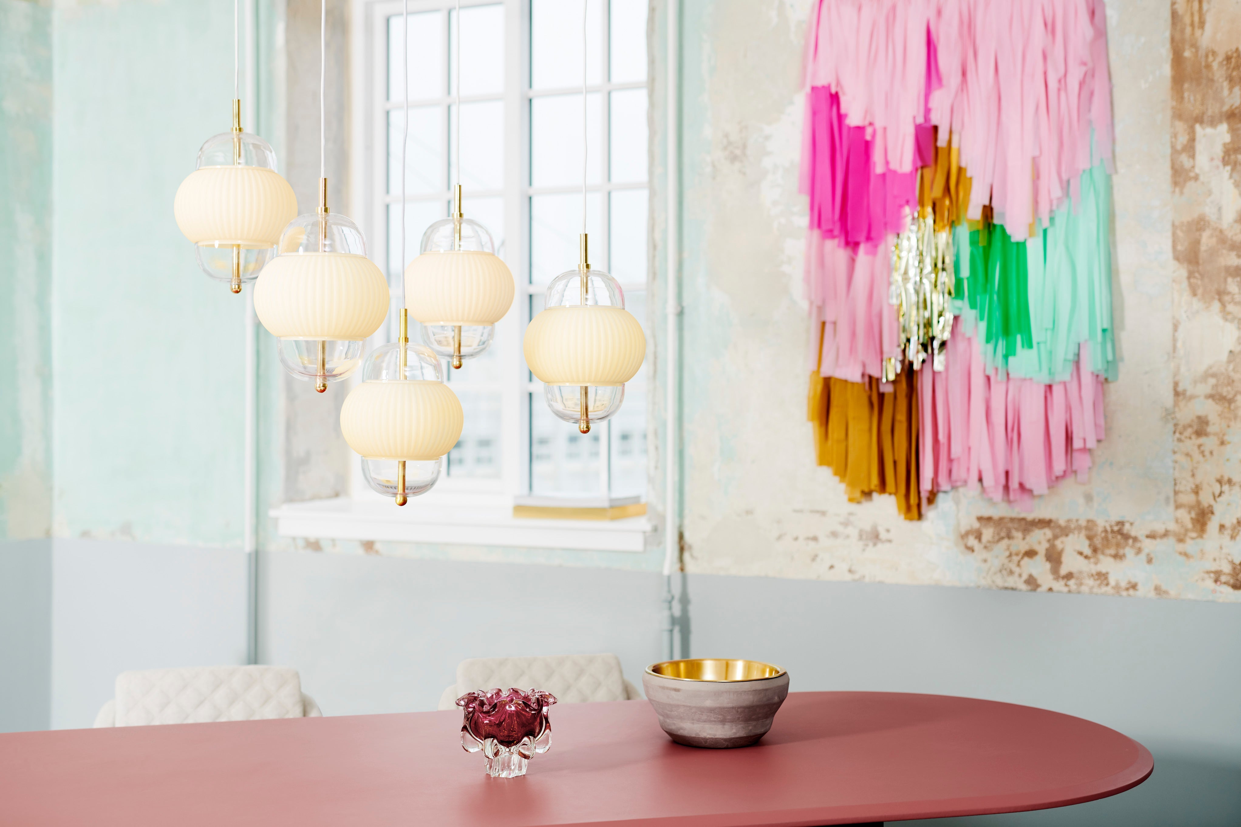 Lampa i klarglas och matt vitt veckat glas. Dessutom har lampan detaljer i mässing och en vit textilkabel.