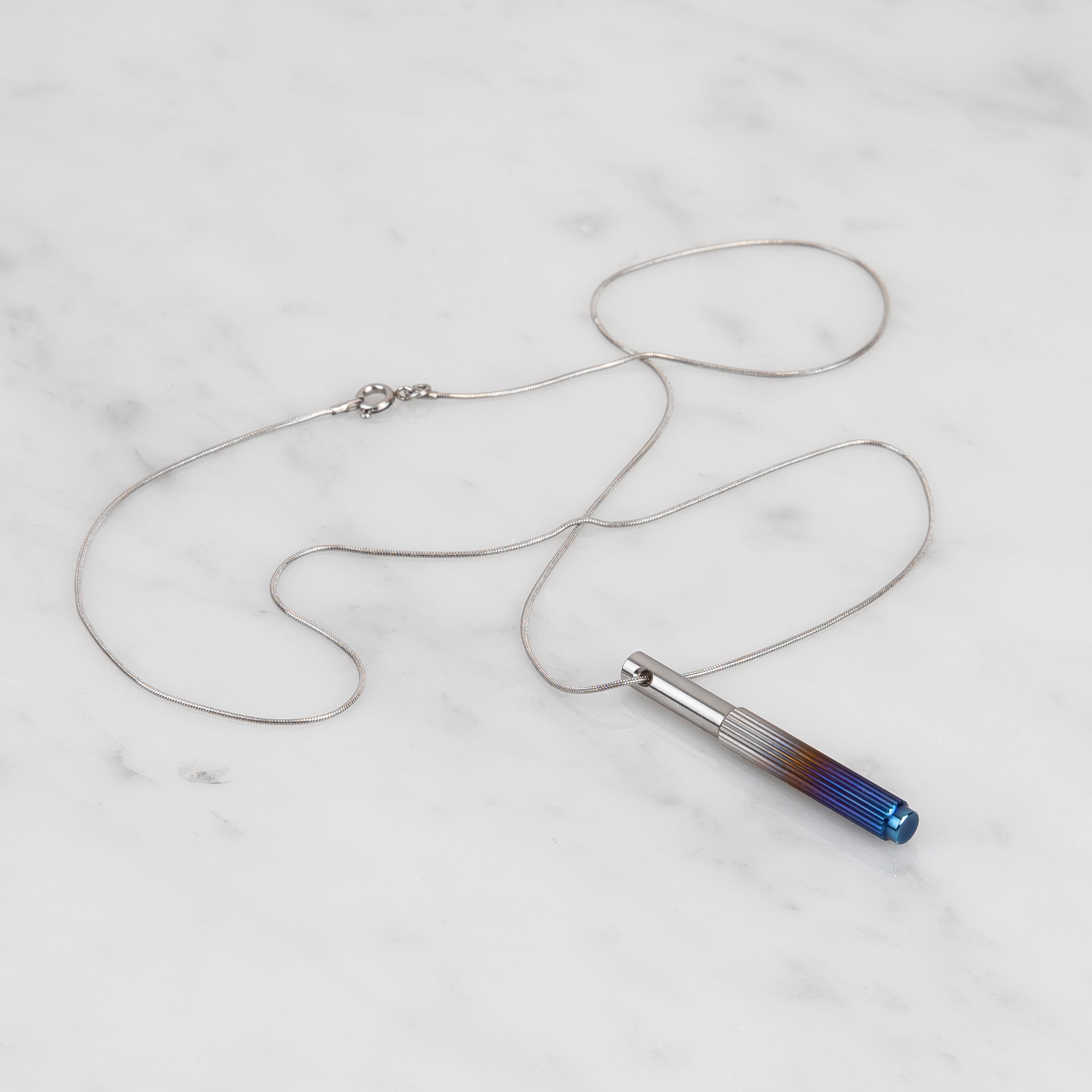 Halsband i stål med hänge i stål och bränt stål. Hänget är dekorerat med ett linjärt mönster.