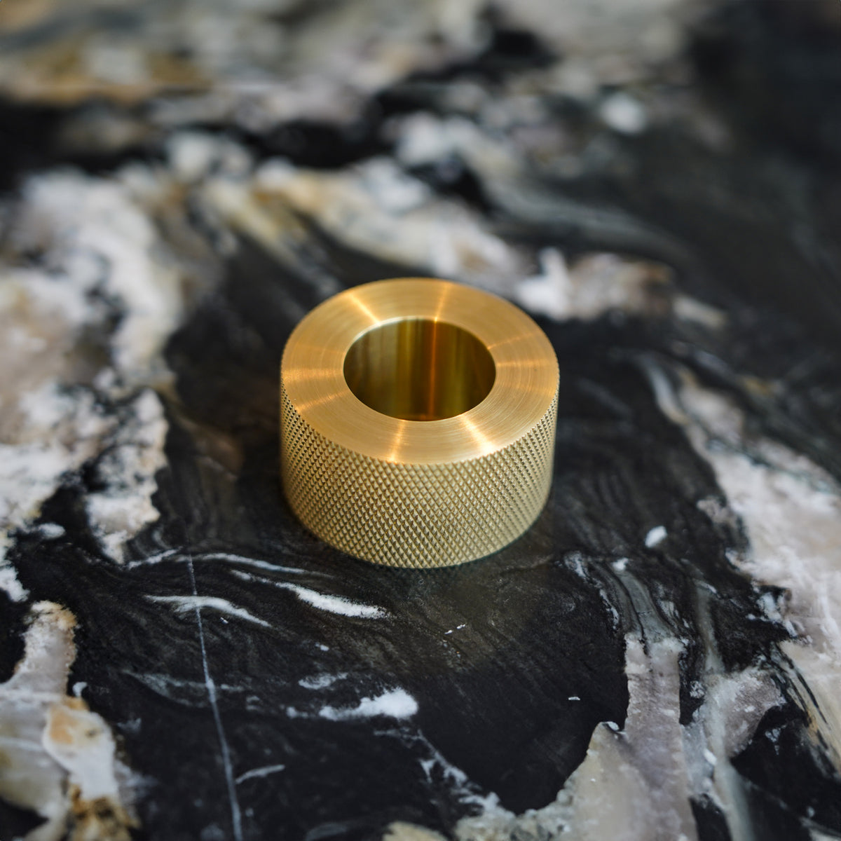 Ringformat Kastellet-handtag i mässing med diamond cut på en mörk stenyta.