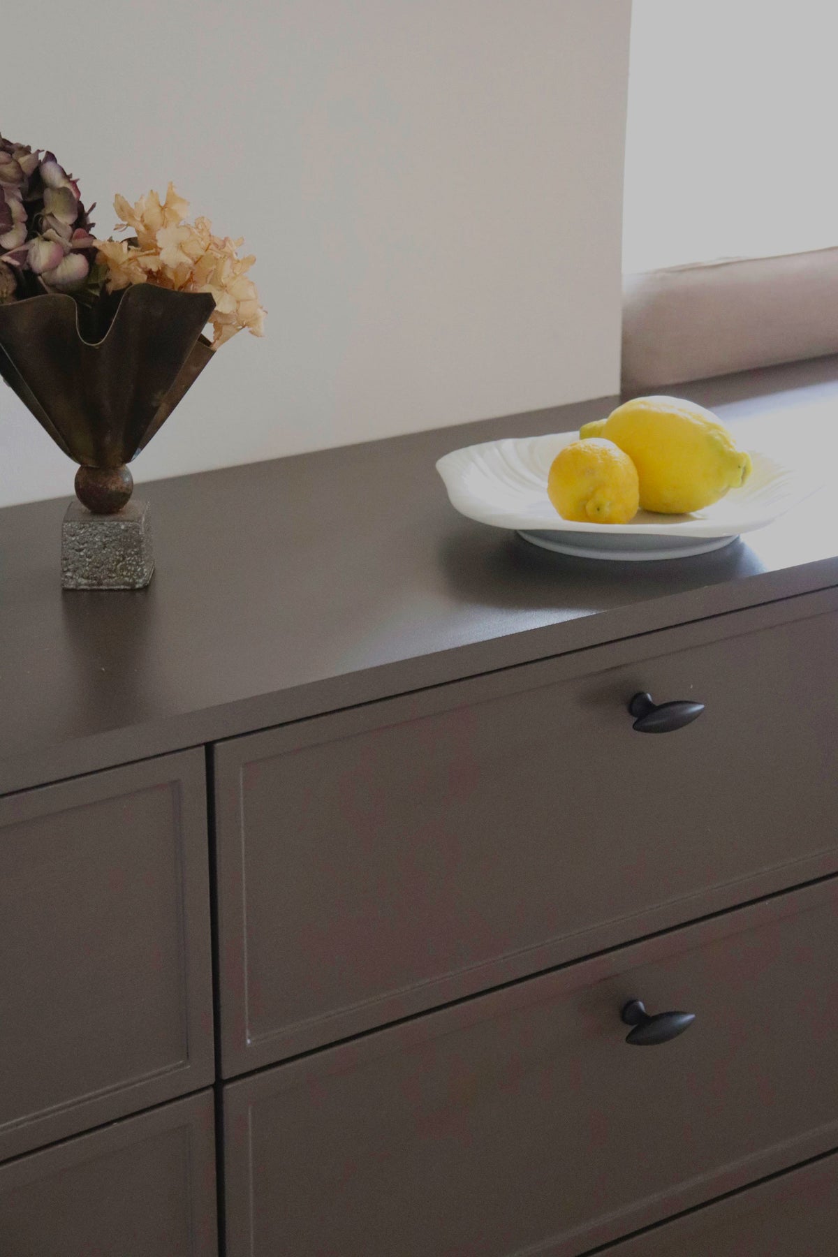 Närbild på Nyholm-knoppar i brunerad mässing på mörka lådor med citroner och blommor ovanpå