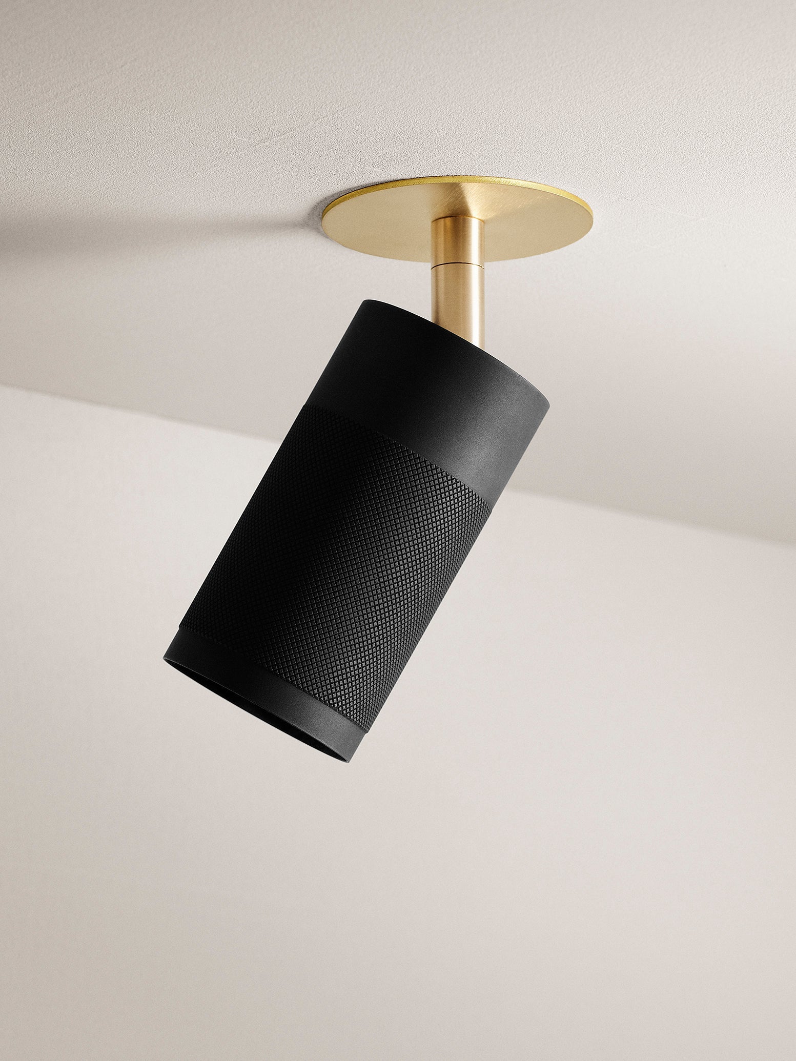 Loftspot af riflet sortbruneret messing og fod i messing, på lyst loft og med lys baggrund.