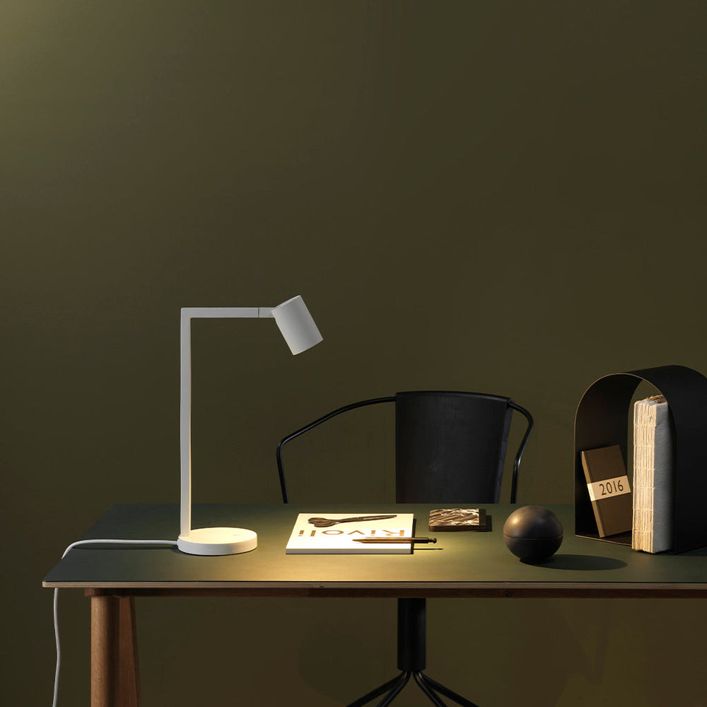 Vit bordslampa med justerbart huvud. Lampan har en enkel design med kantiga linjer/vinklar.