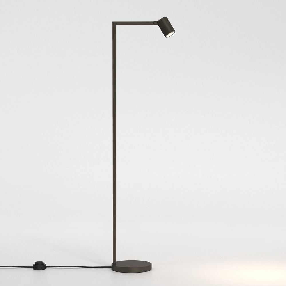 Golvlampa i bronsfärgat stål med justerbart huvud. Lampan har en enkel design med kantiga vinklar och en rund fot.