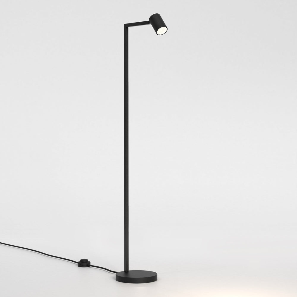 Golvlampa i svart stål med justerbart huvud. Lampan har en enkel design med kantiga vinklar och en rund fot.