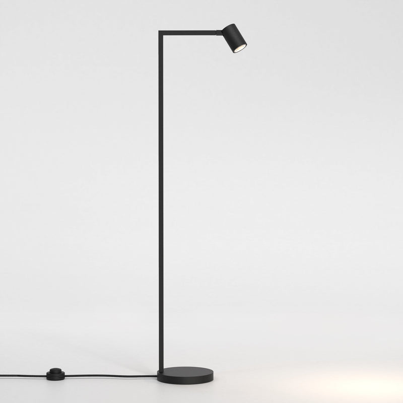 Golvlampa i svart stål med justerbart huvud. Lampan har en enkel design med kantiga vinklar och en rund fot.