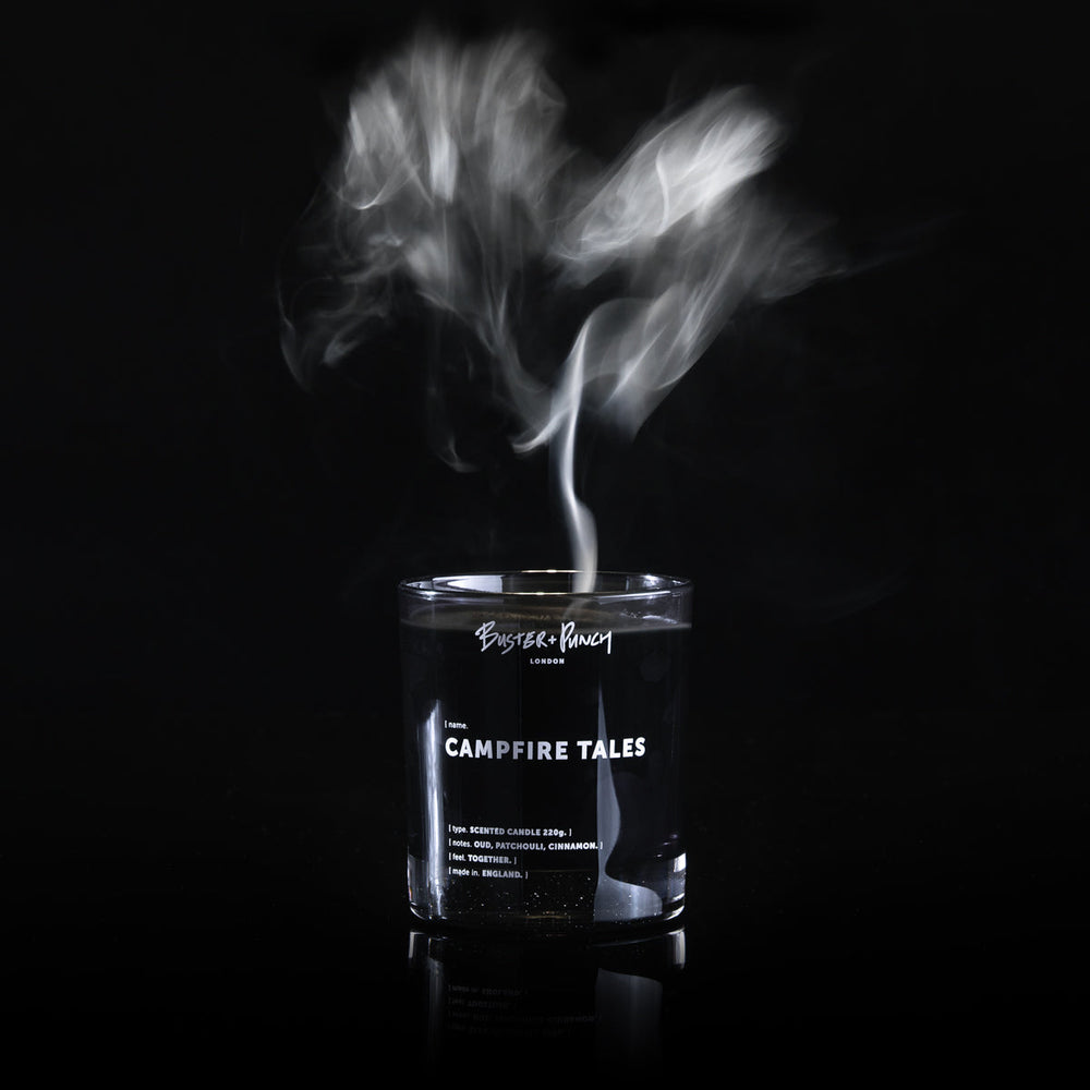 Doftljus av svart vax i rökfärgat glas med rök från en låga, mot svart bakgrund.