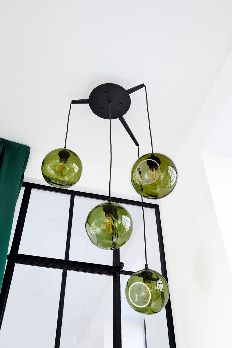 Rund lampa i grönt glas med en avskuren bit som ger en skymt av glödlampan. Sockeln är svart och kabeln av svart textil.