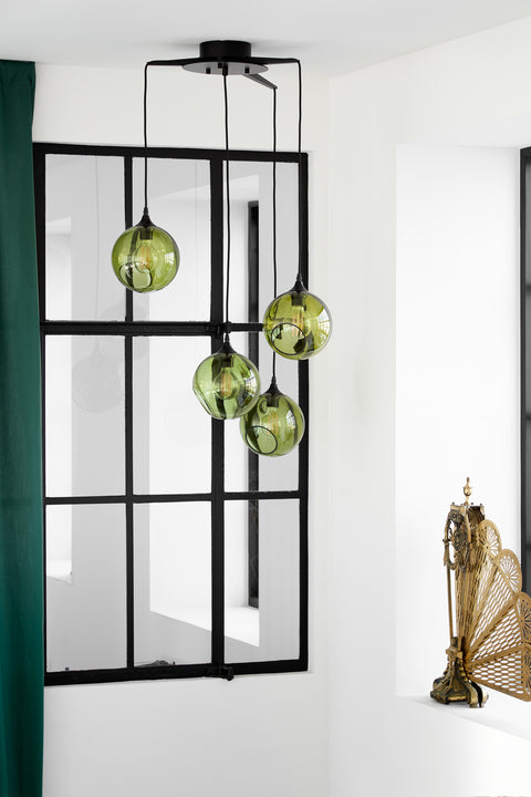 Rund lampa i grönt glas med en avskuren bit som ger en skymt av glödlampan. Sockeln är svart och kabeln av svart textil.