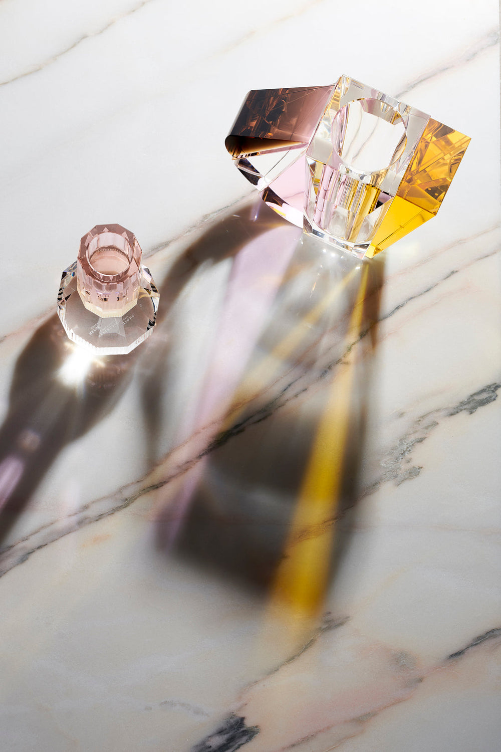Vas och ljusstake i färgad kristall sedd ovanifrån på ett marmorbord.