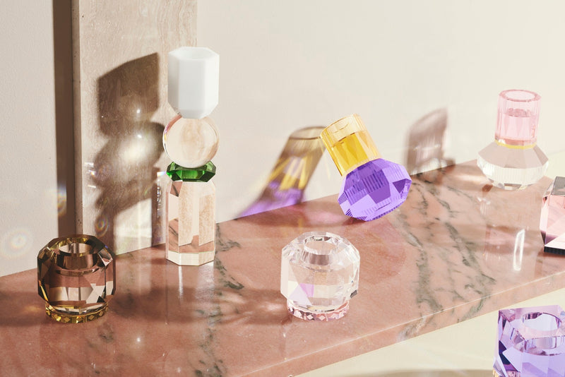 Set med olika värmeljusljusstakar i färgat kristallglas, placerade på en laxfärgad marmorplatta.