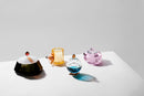 Fyra olika doftljus i färgad kristall, stående på ett vitt bord med vit bakgrund.