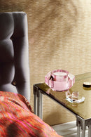 Doftljus i en rosa kristallbehållare, stående på ett nattduksbord av glas.