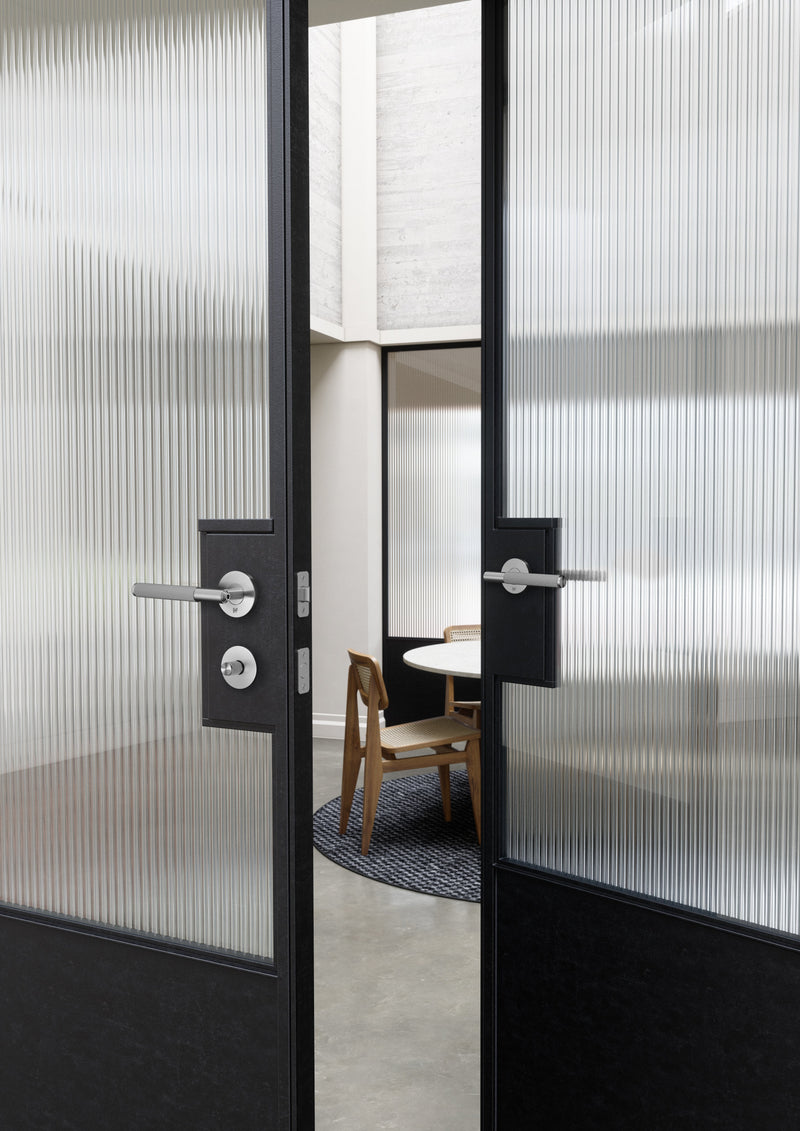 Dörrhandtag i rostfritt stål i en rå och exklusiv look med linjerat mönster. Här visas dörrhandtaget monterat på en ståldörr med glasruta.