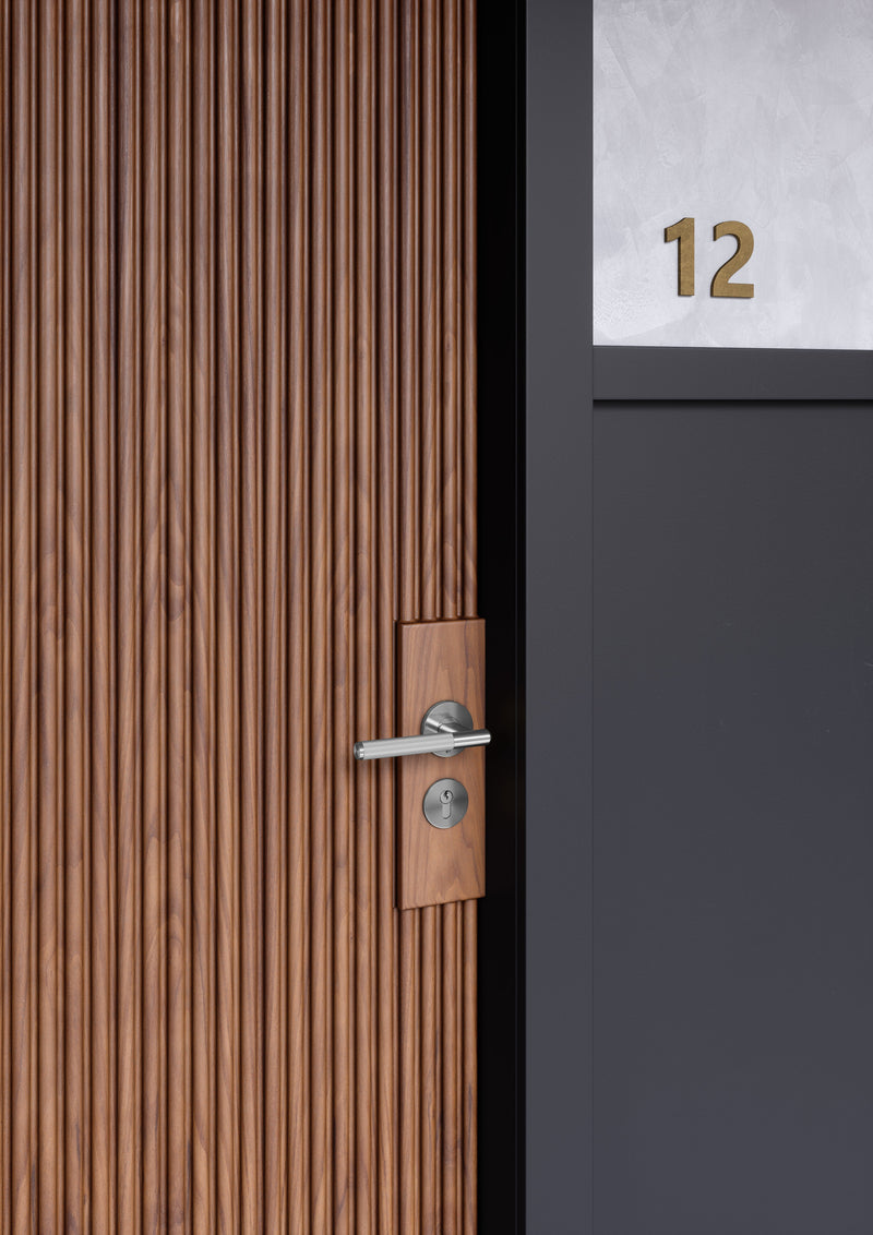 Dörrhandtag i rostfritt stål i en rå och exklusiv look med linjerat mönster. Här visas dörrhandtaget monterat på en trädörr.