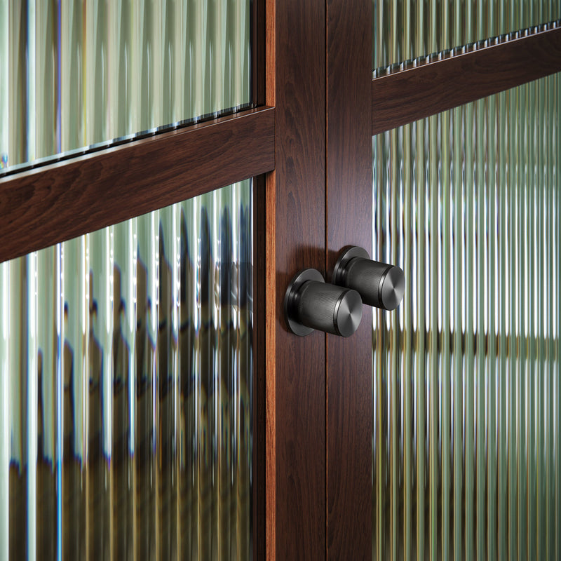 Exklusiv dörrknopp i gun metal med linjerat mönster. Här visas två dörrknoppar monterade på en trädörr med glasrutor.