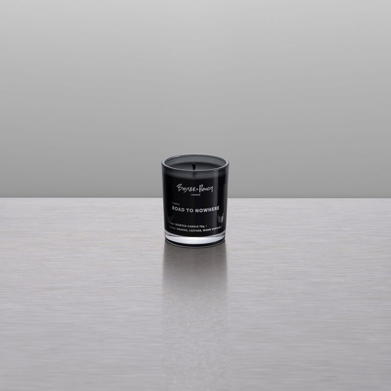 Doftljus av svart vax i rökfärgat glas, mot grå bakgrund.
