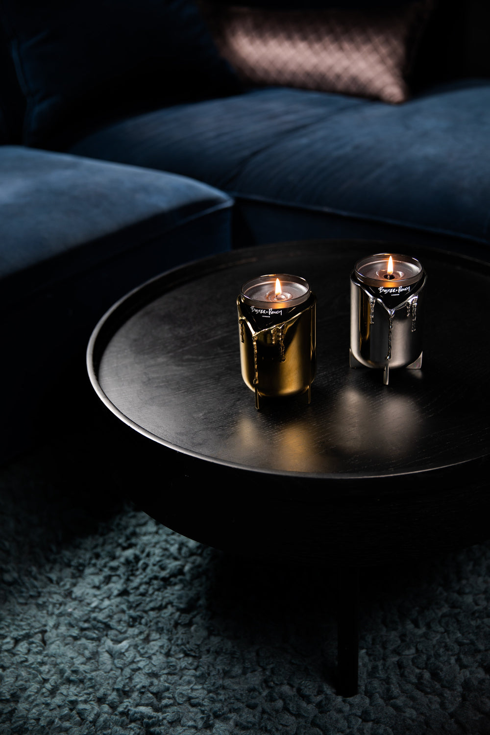 2 ljusstakar i stål och mässing med doftljus i glas, på ett svart soffbord