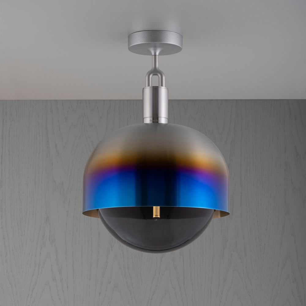 Taklampa med fattning i stål samt skärm i bränt stål och ljuskälla i rökfärgat glas, mot en grå bakgrund.