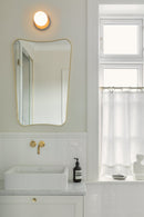 Væglampe med lampeskærm af opalglas og gylden fatning, ved spejl på badeværelse