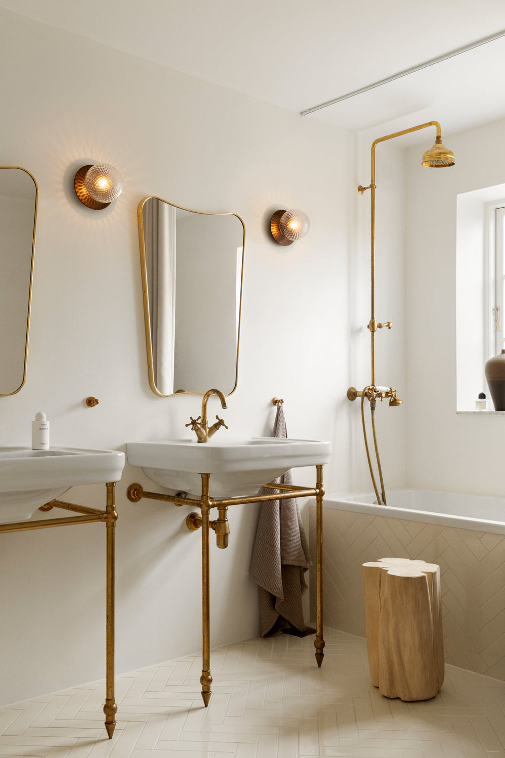 To væglampe med lampeskærme af klart optikglas og gylden fatning, hængende ved spejl på badeværelse