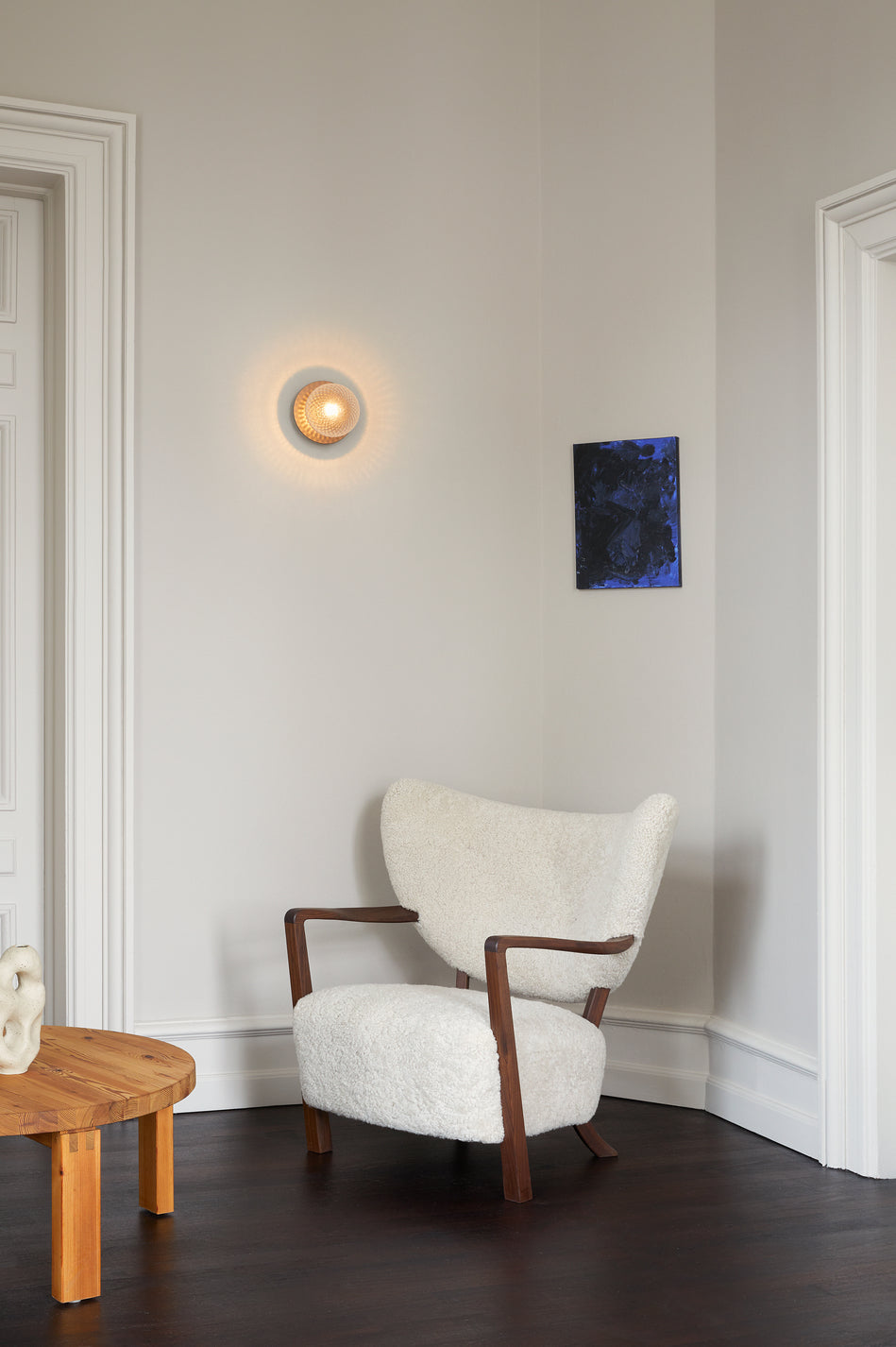 Væglampe med lampeskærm af klart optikglas og gylden fatning, hængende i dagligstuemiljø