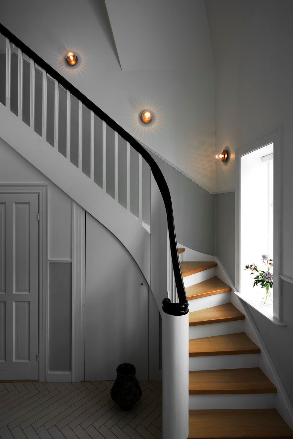 Tre væglampe med lampeskærme af klart optikglas og gylden fatning, hængende langs trappe i hall