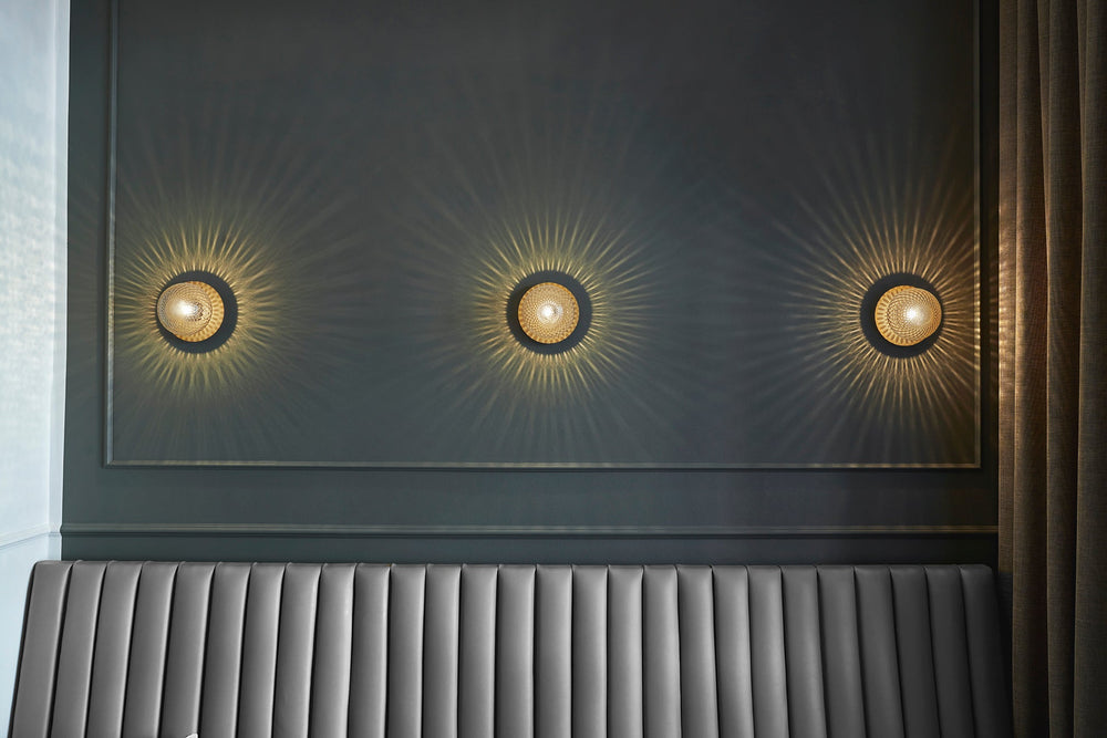 Tre væglamper med lampeskærme af klart optikglas og gylden fatning, over sofa