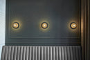Tre væglamper med lampeskærme af klart optikglas og gylden fatning, over sofa