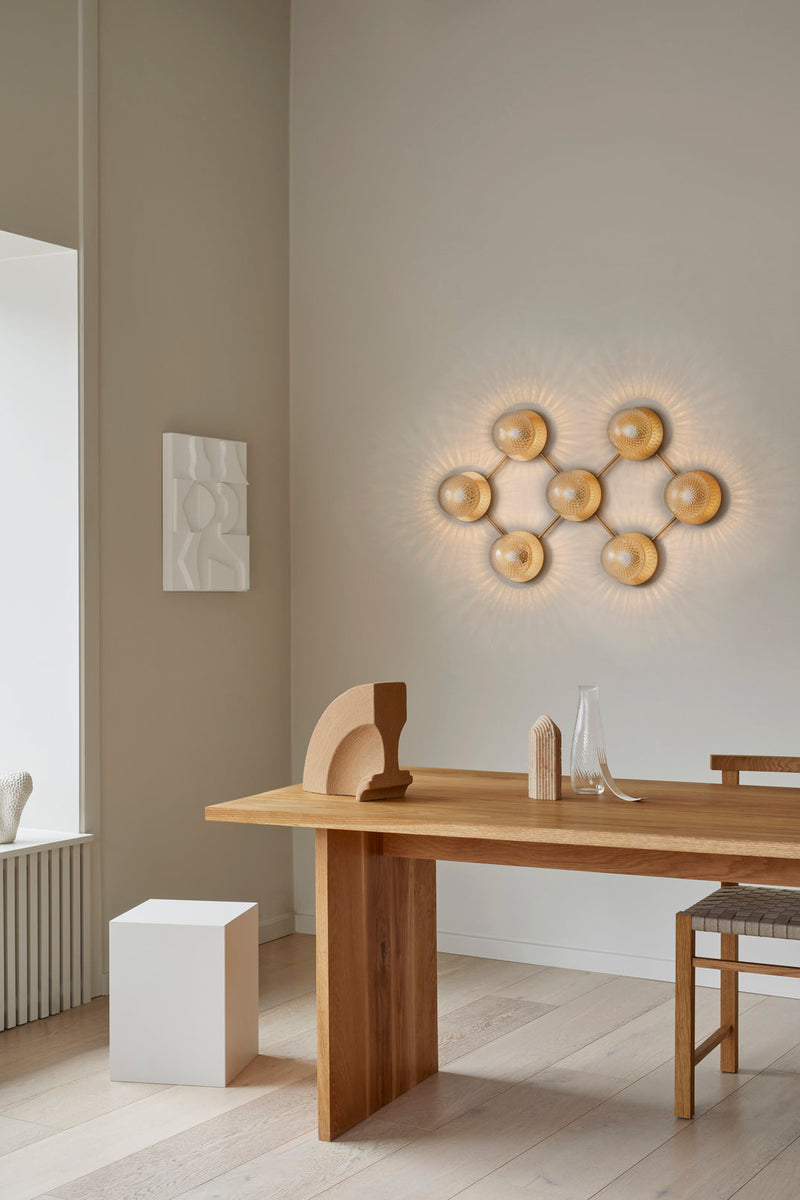 Væglampe med lampeskærme af klart optikglas og gylden fatning og stel, hængende i dagligstuemiljø