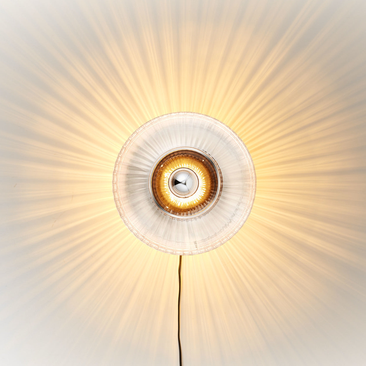 Rund vägglampa i klart veckat glas som skapar ett ljusspel på väggen. 