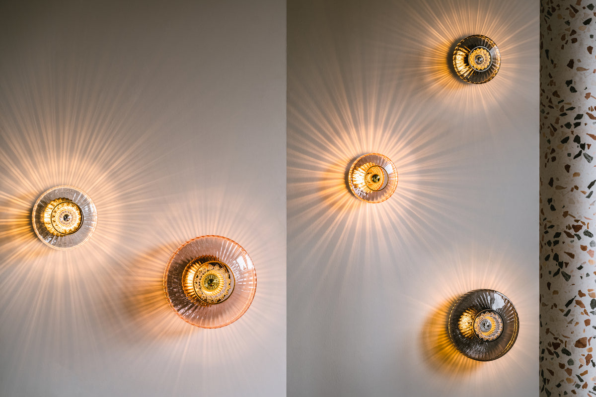 Rund vägglampa i klart veckat glas som skapar ett ljusspel på väggen.