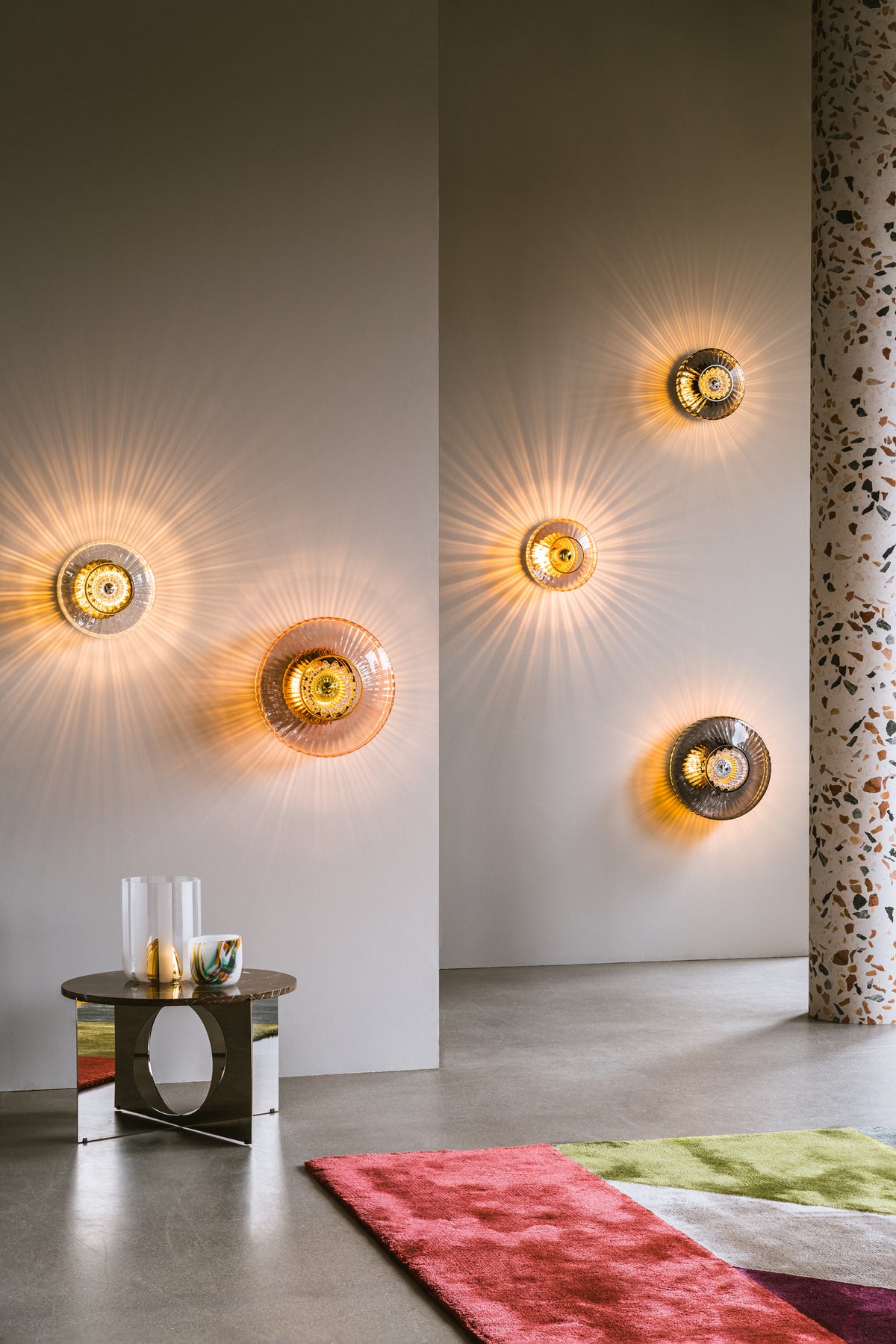 Rund vägglampa i rosa veckat glas som skapar ett ljusspel på väggen.
