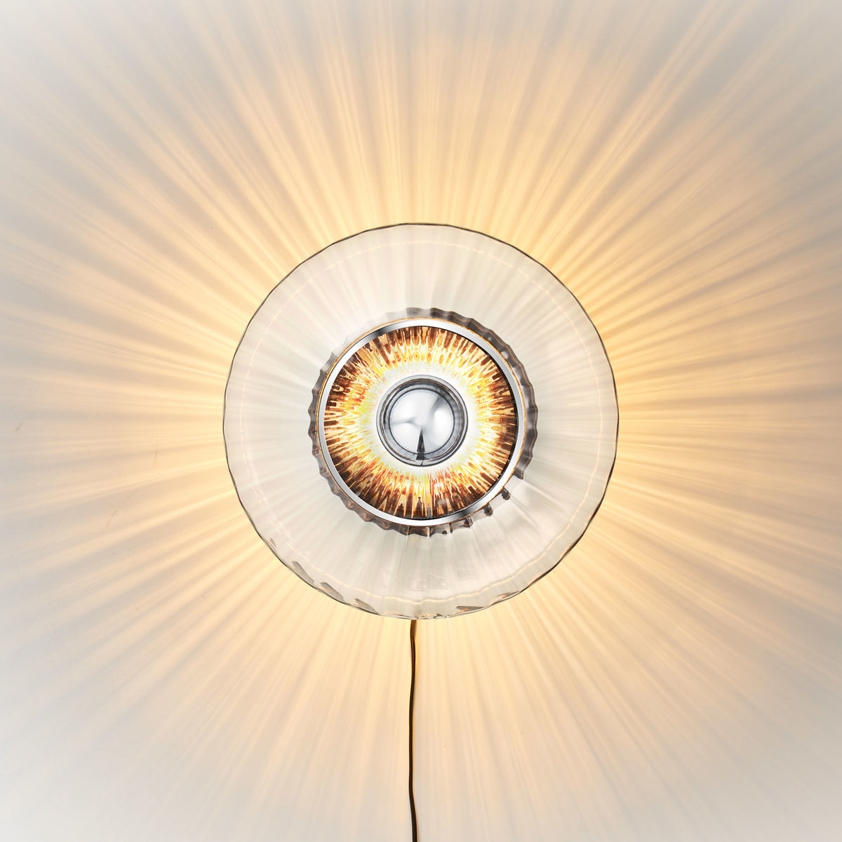 Rund vägglampa i klart veckat glas som skapar ett ljusspel på väggen.
