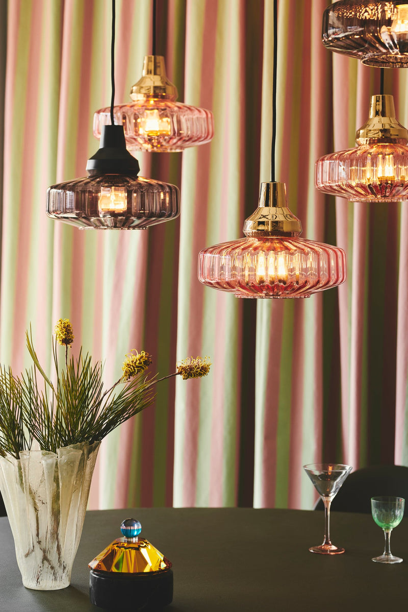 Pendel från Design by Us i rosa glas och med guldfärgad sockel och baksida.