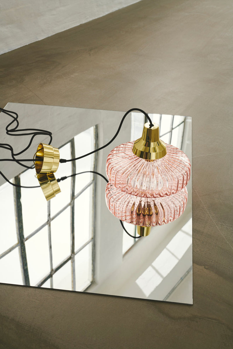 Pendel från Design by Us i rosa glas och med guldfärgad sockel och baksida.
