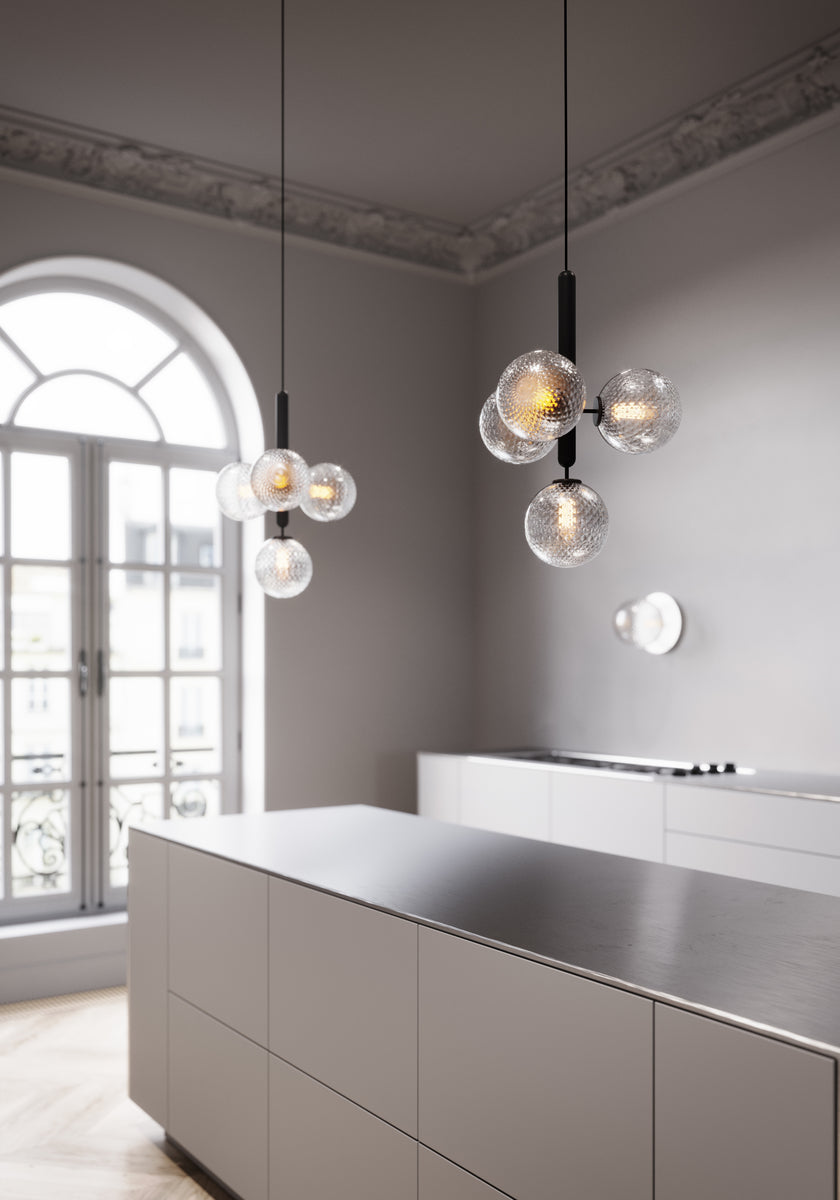 Tre væglamper med lampeskærme af klart optikglas og sølvfarvet fatning, hængende i køkken over køkkenbord