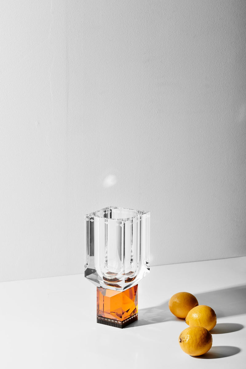 Vas i klart och bärnstensfärgat kristallglas stående på ett vitt bord tillsammans med tre citroner.