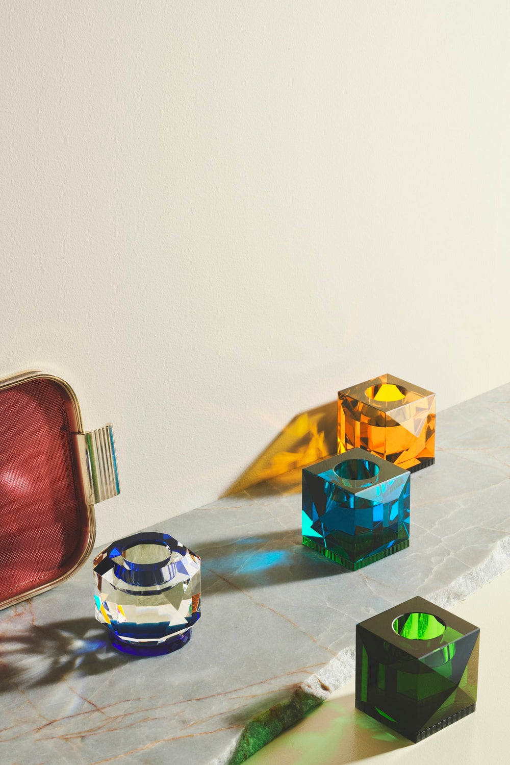 Fyra olika värmeljusstakar i färgad kristall, på en marmorplatta.
