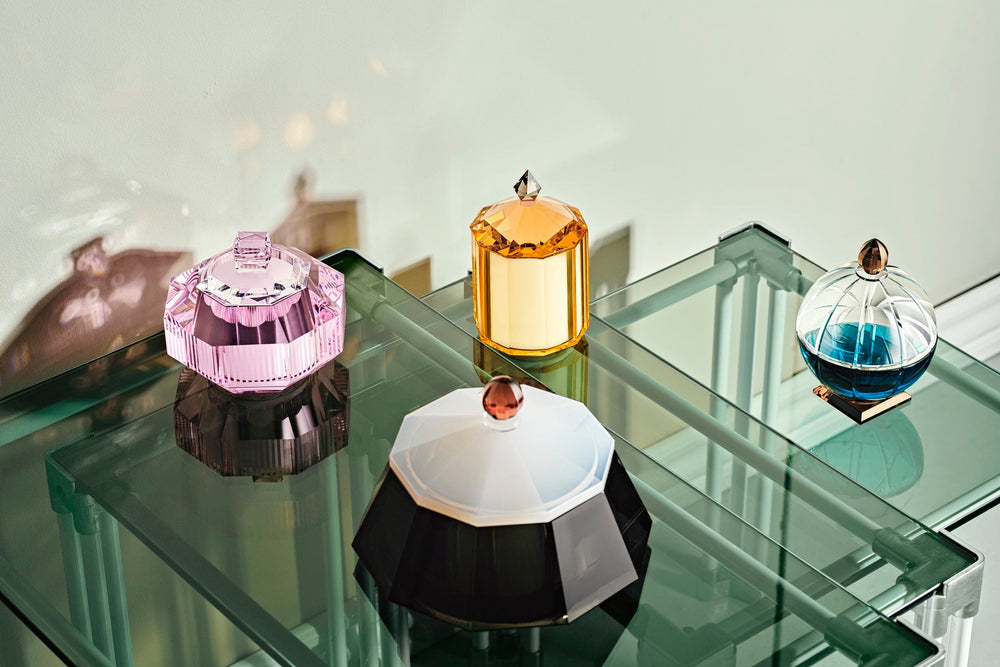 Fyra olika doftljus i färgad kristall som står på satsbord i glas.