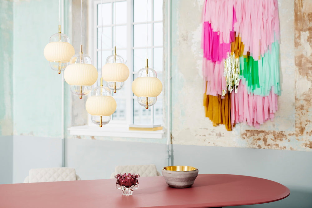 Lampa i klarglas och matt vitt veckat glas. Dessutom har lampan detaljer i mässing och en vit textilkabel. 