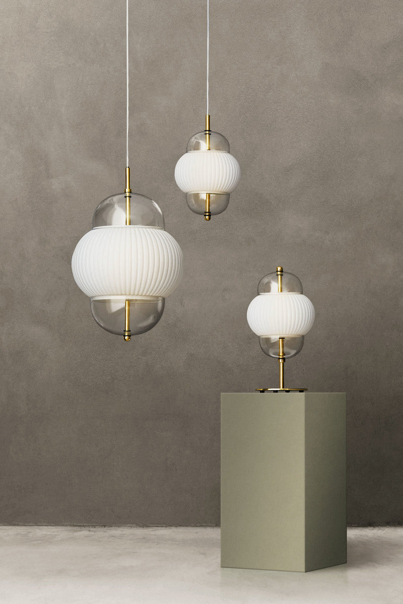 Lampa i klarglas och matt vitt veckat glas. Dessutom har lampan detaljer i mässing och en vit textilkabel. 