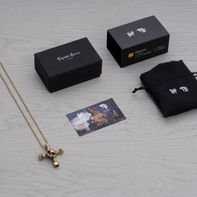 Kartong som innehåller halsband med hänge i form av en dödskalle som samtidigt är en trumnyckel, i mässing
