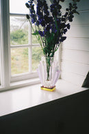 Vas i klar, rosa, lila och gul kristall med blommor i, stående på en vit fönsterbräda.